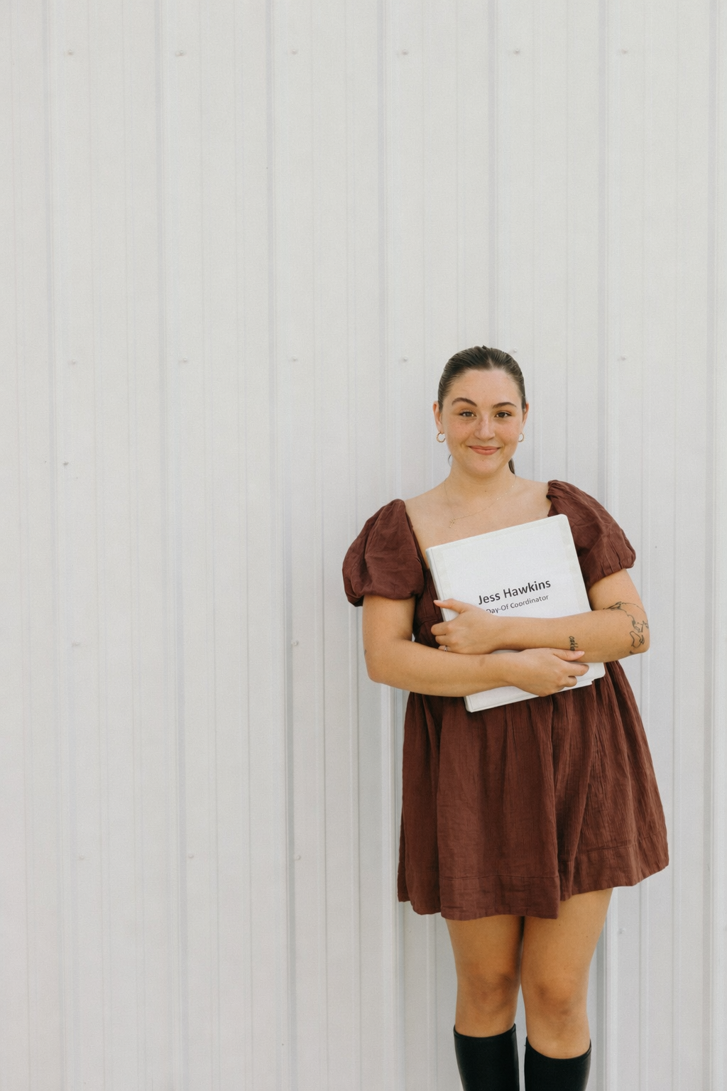 Jess Hawkins standing in a rust dress and holding a wedding coordinator portfolio.